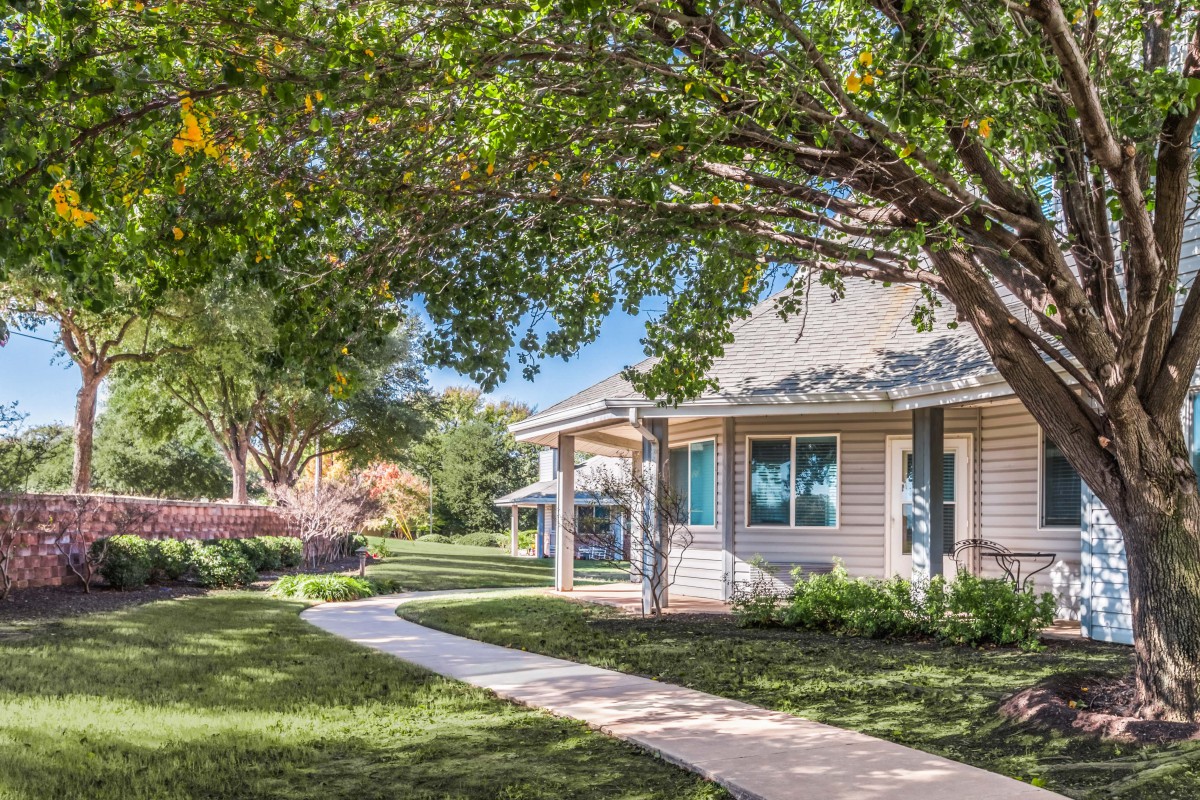 A charming house with a well-kept lawn and a pathway, surrounded by trees on a sunny day.