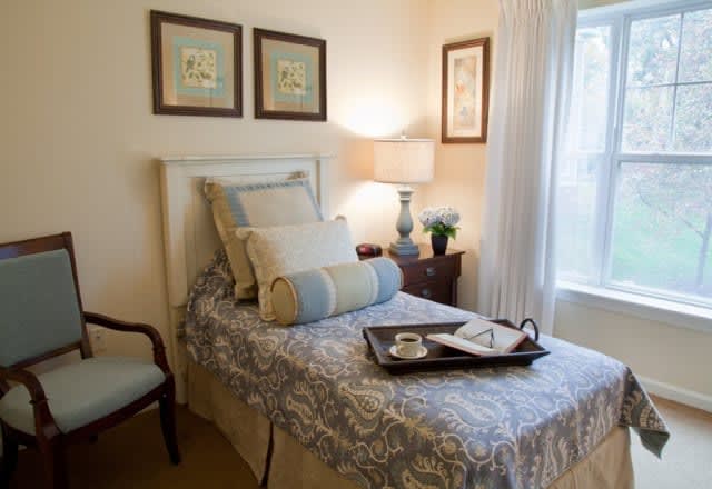 A cozy bedroom with a single bed decorated with pillows and a tray, accompanied by a side table and lamp.
