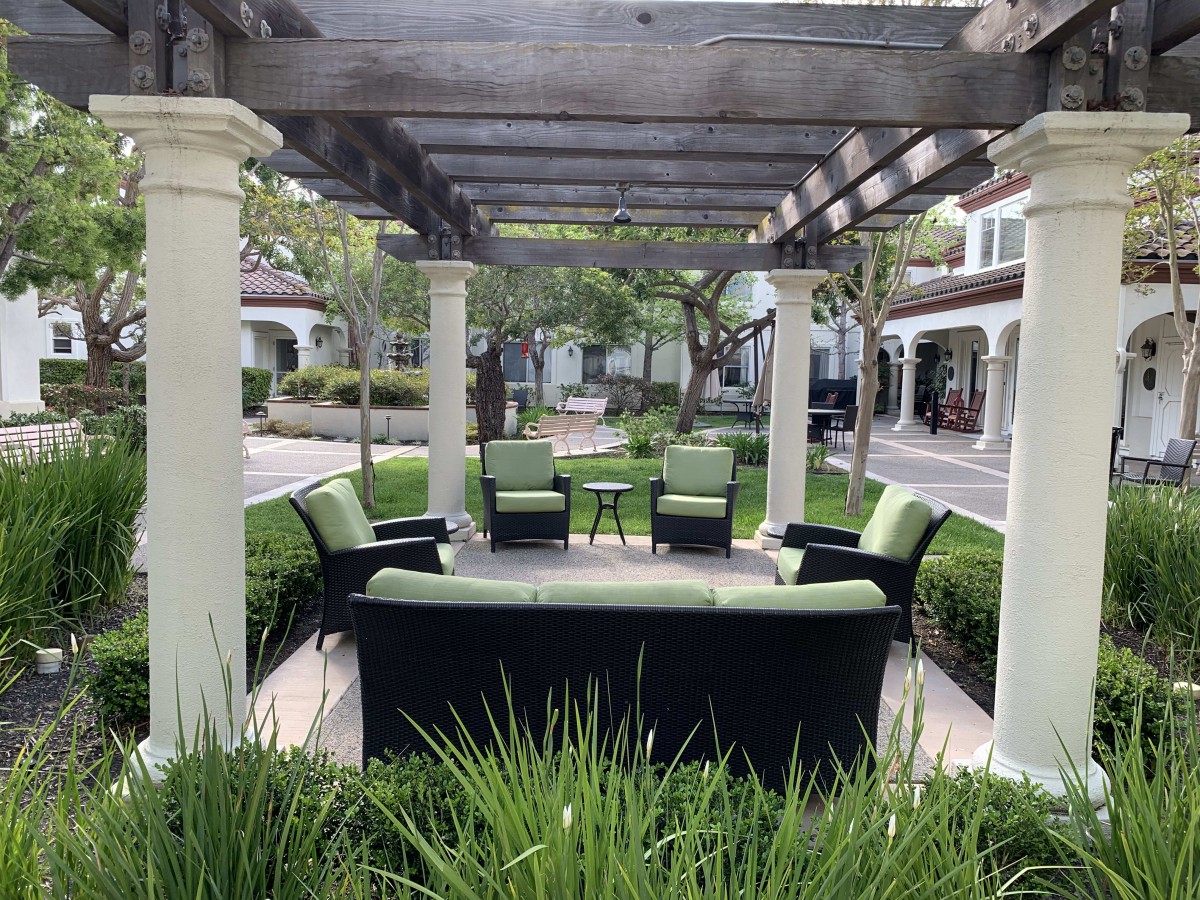 An inviting outdoor seating area under a pergola, surrounded by lush greenery and landscaped gardens.