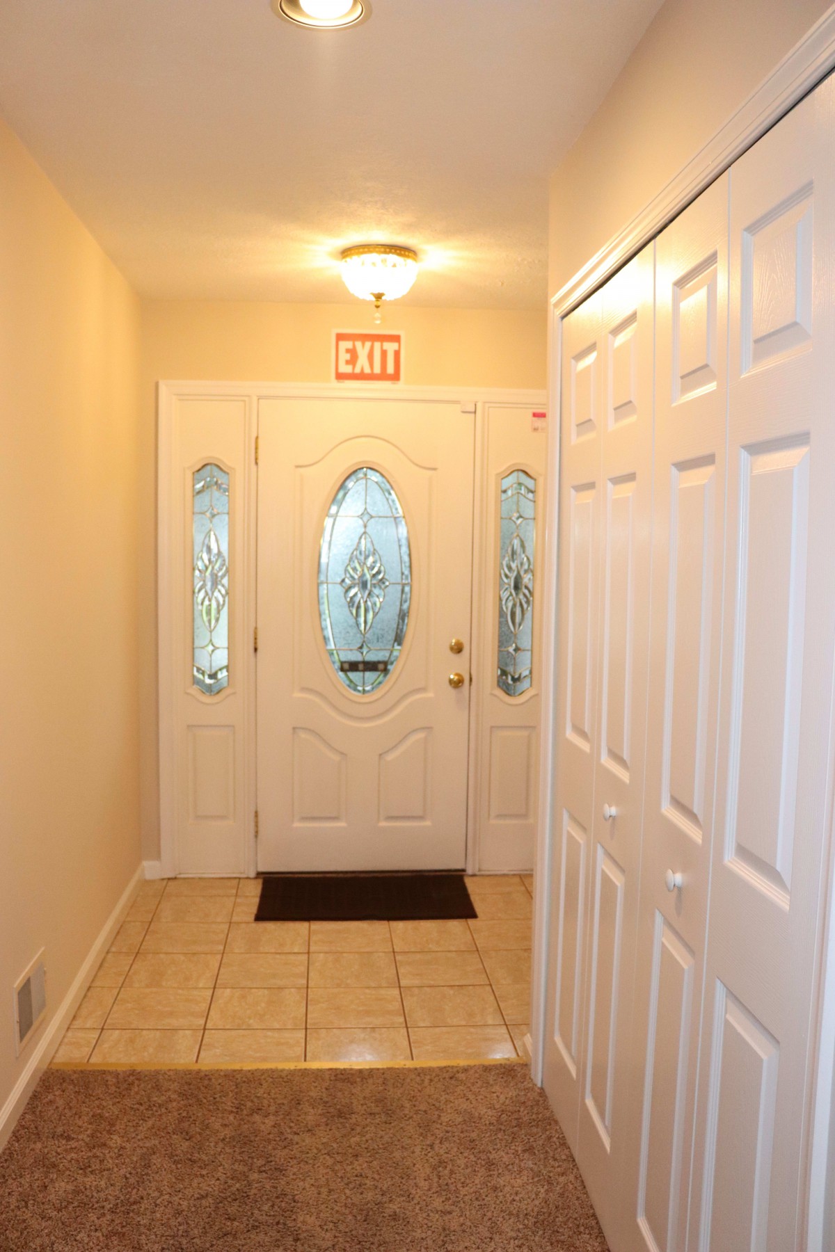 A well-lit hallway with an ornate entrance door and tile flooring.