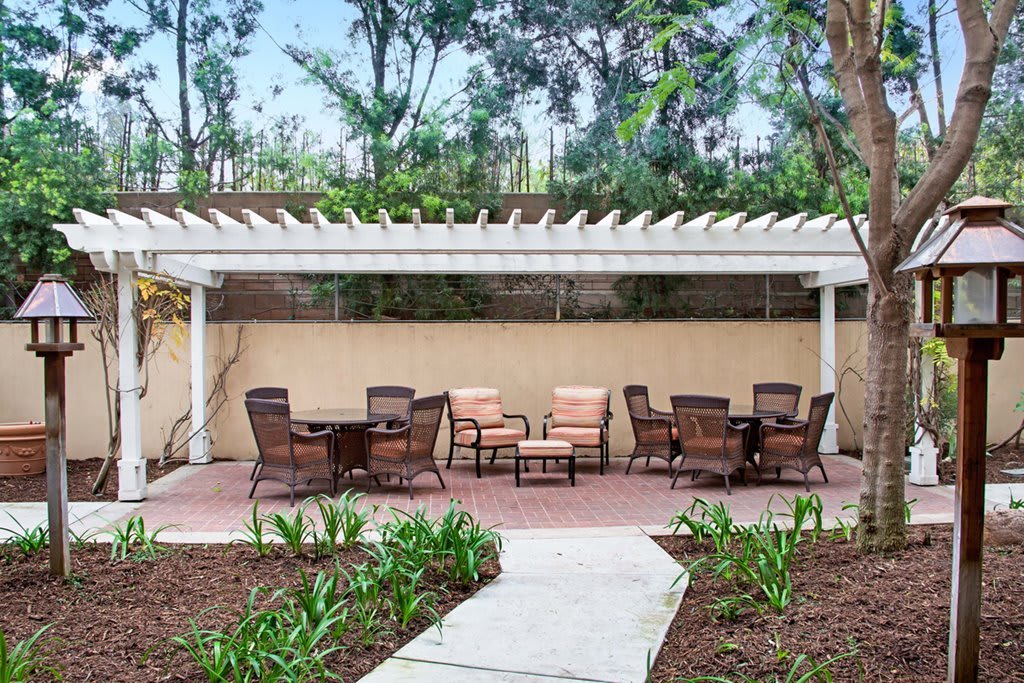 A peaceful garden setting featuring a pergola with outdoor seating and lush greenery.