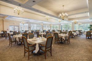 An elegant dining room with neatly arranged tables and chairs, illuminated by chandeliers.