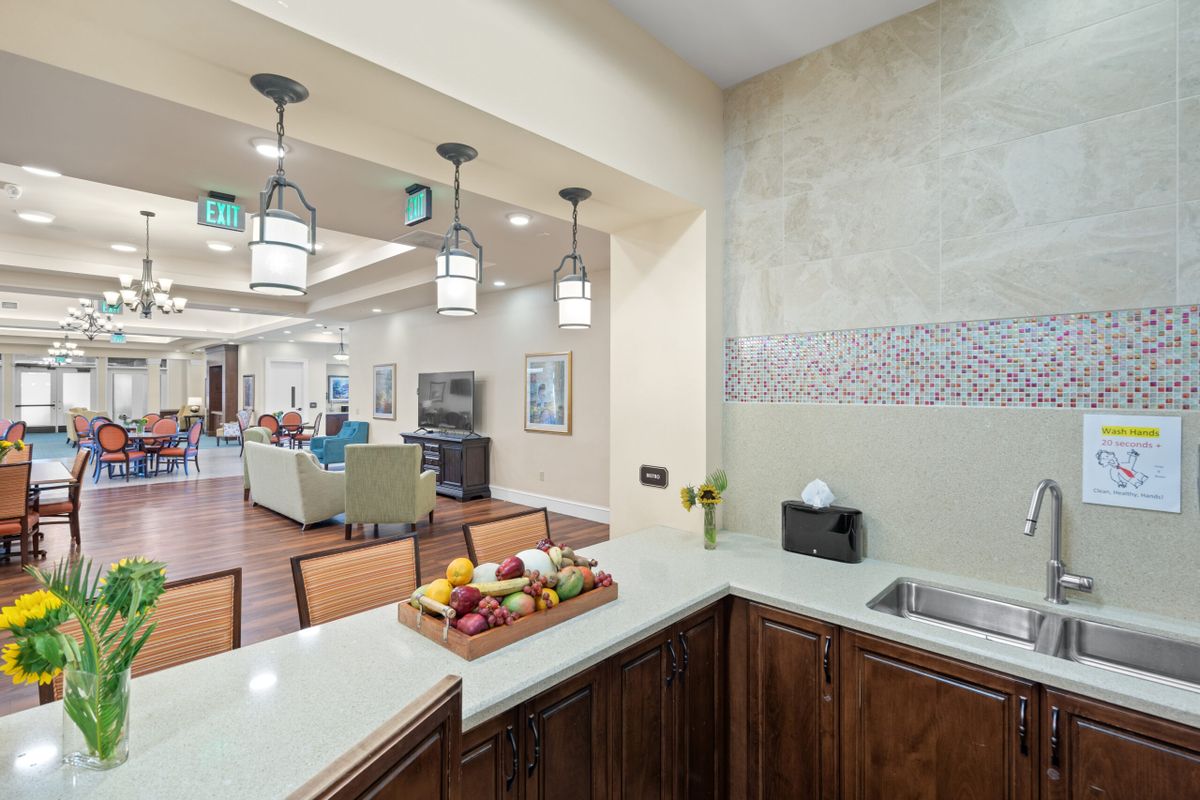 A modern kitchen area opens up to a living space, featuring stylish lighting and a fruit basket on the counter.