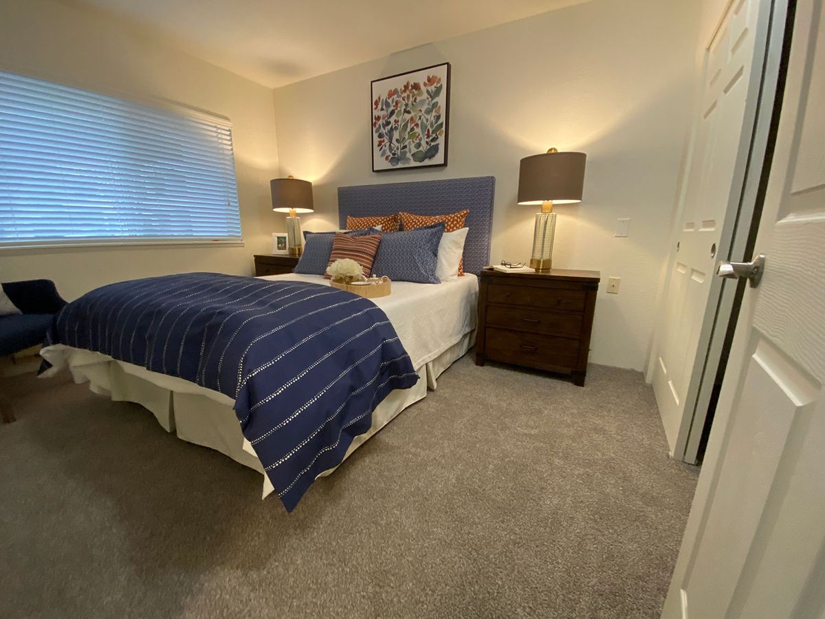 A cozy and modern bedroom with a blue-themed decor, featuring a comfortable bed, two lamps on wooden nightstands, and a decorative painting above the headboard.