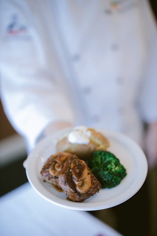 A chef presenting a gourmet dish with meat, mashed potatoes, and greens.