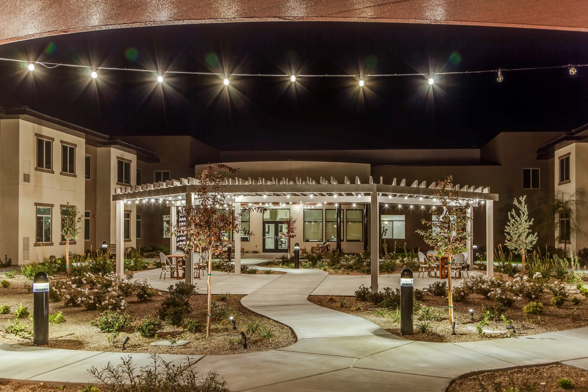 A beautifully lit outdoor area at night featuring a pergola and string lights along a landscaped pathway.