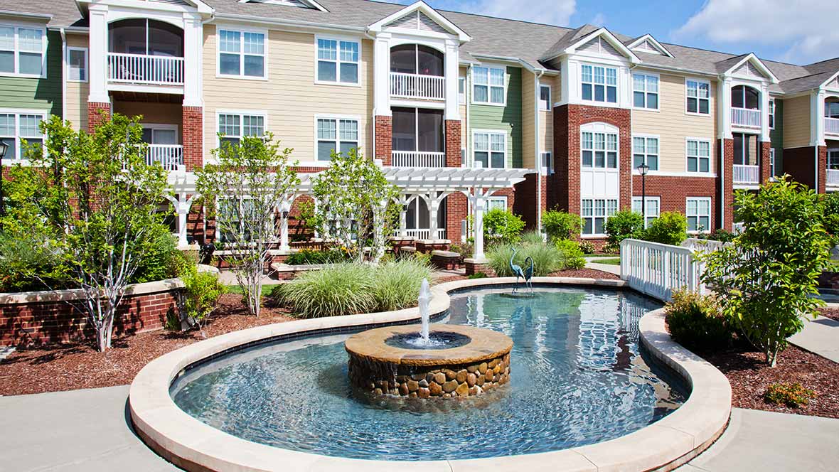 A modern apartment complex with a landscaped courtyard featuring a fountain.