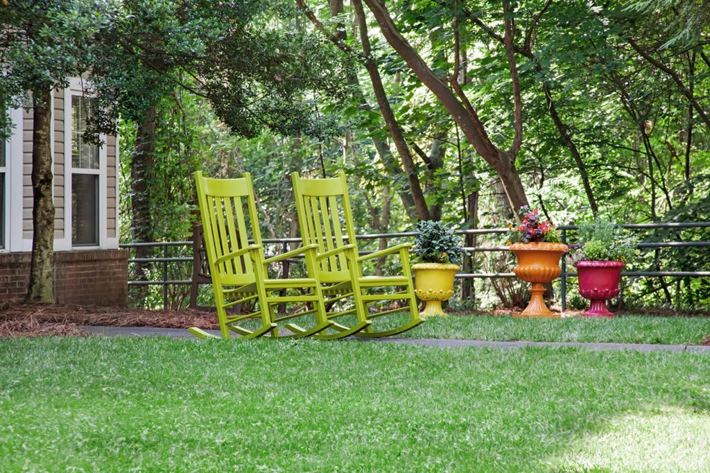 Two bright yellow rocking chairs sit in a lush garden surrounded by trees and potted plants.