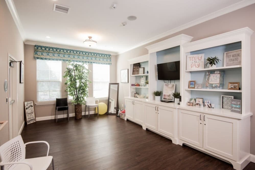 A modern living room with built-in shelves, a television, and wood flooring illuminated by natural light.