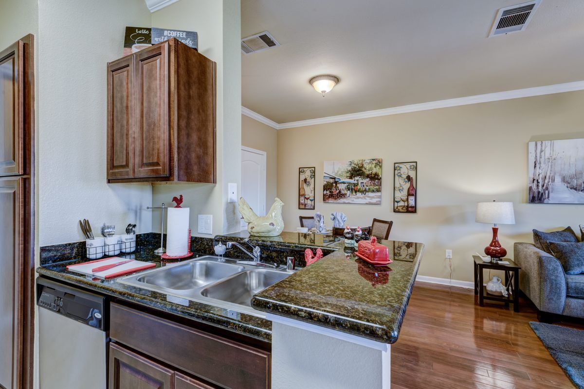 A modern kitchen with a view into the living area, featuring wooden cabinets and a granite countertop.