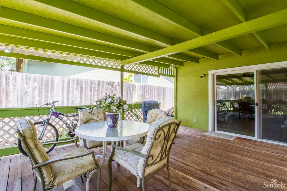 A cozy patio with a green-painted ceiling, featuring a table and chairs on a wooden deck, next to a bicycle.