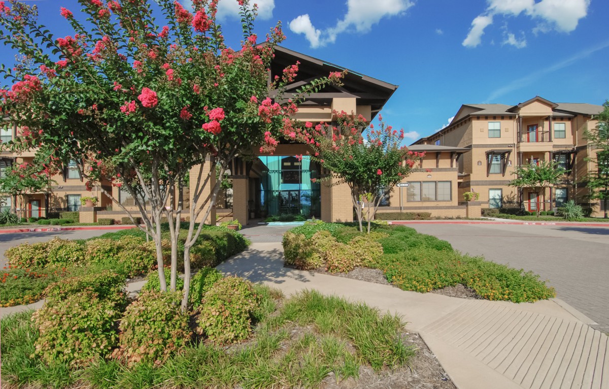 A scenic view of a modern building surrounded by lush landscaping and vibrant flowers under a clear blue sky.