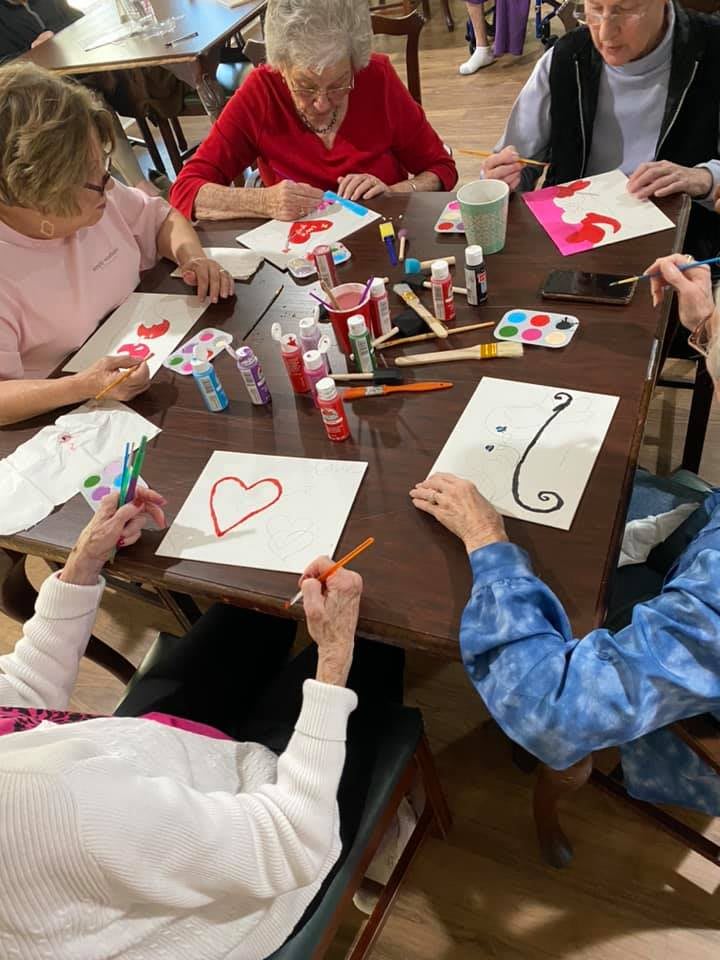 A group of people engaging in a painting activity, creating heart and swirl designs on paper at a table.