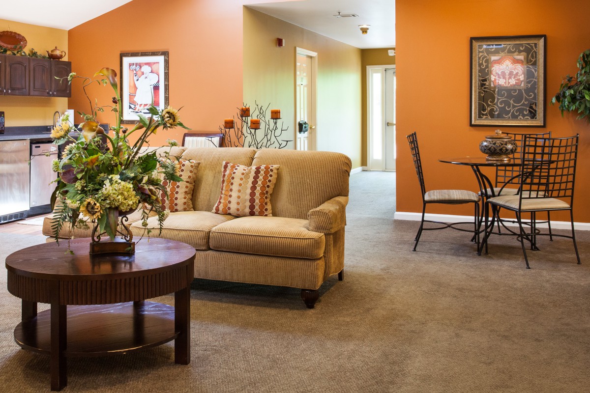 A cozy living room with an orange accent wall, featuring a comfortable sofa and a small dining area.