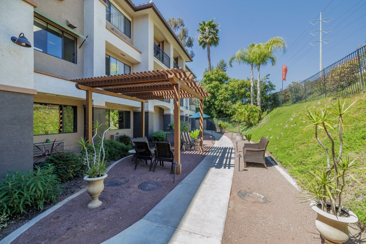 An apartment building with a landscaped patio area featuring a pergola, outdoor seating, and lush greenery.
