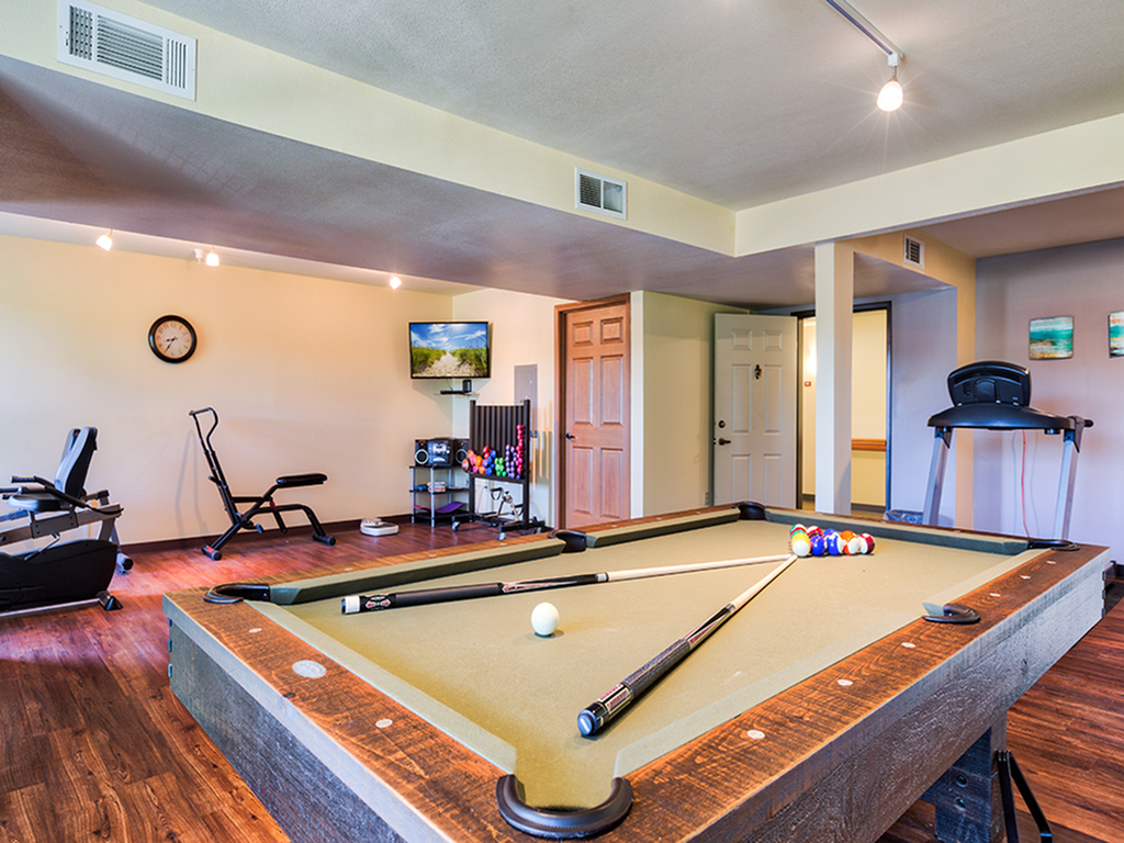 A well-equipped game room featuring a pool table, exercise equipment, and a television.