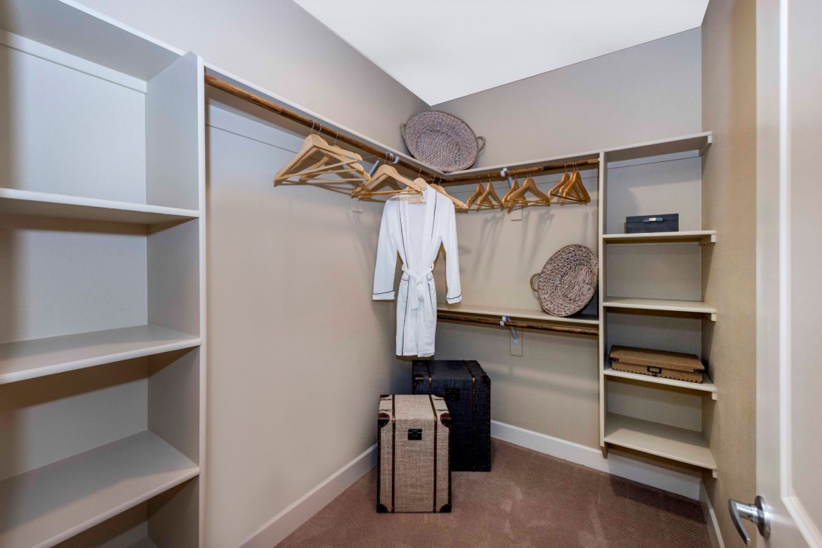 An organized walk-in closet featuring shelves, hangers, a robe, and luggage.