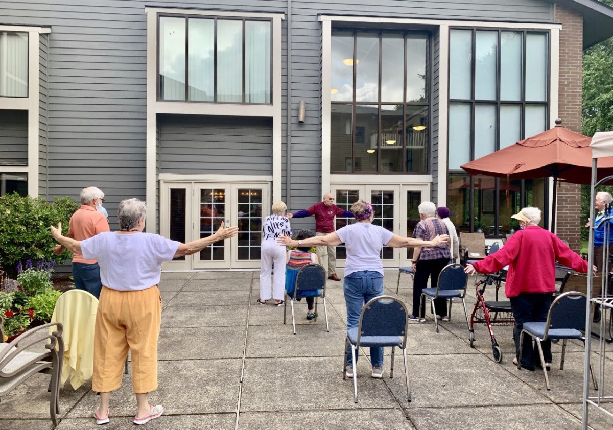 A group of elderly individuals participating in an outdoor exercise session on a patio.