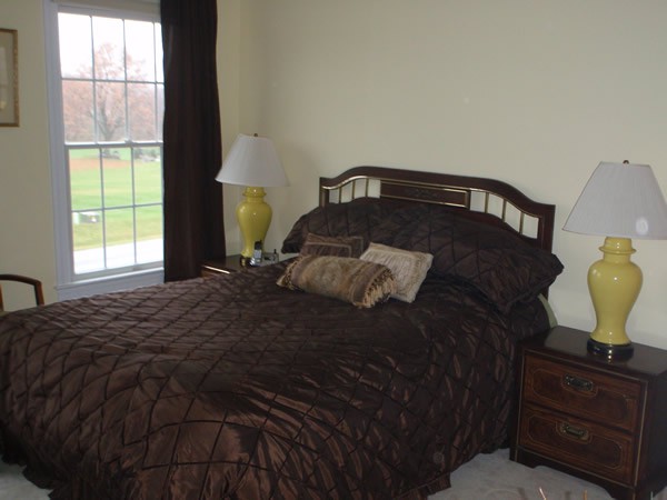 A cozy bedroom with a neatly made bed, pillows, and a lamp by the window.