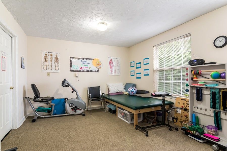A physical therapy room equipped with exercise equipment, a therapy table, and medical posters on the walls.