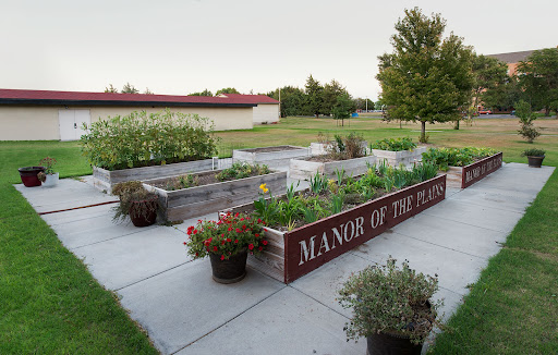 A well-maintained community garden featuring raised vegetable beds at the Manor of the Plains, surrounded by greenery.