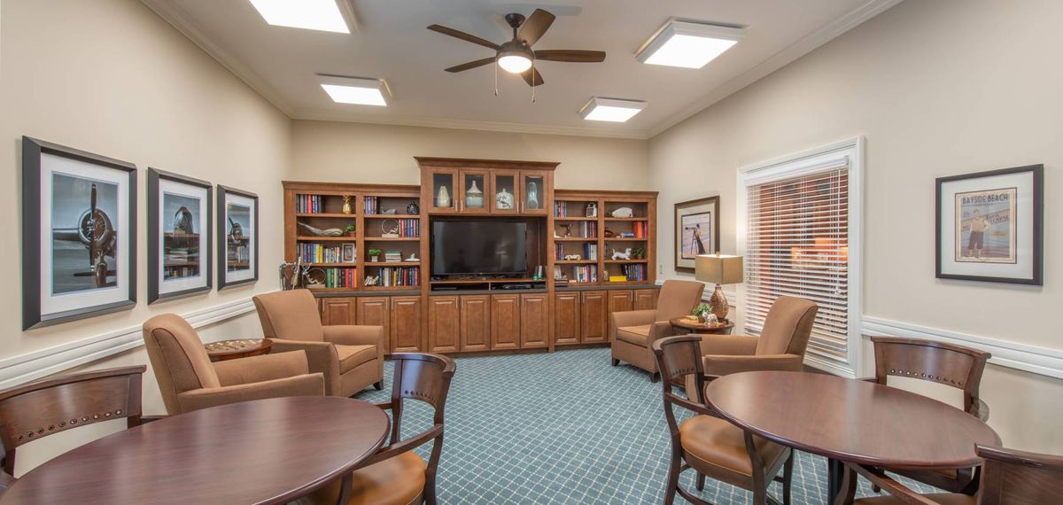 A cozy library room with bookshelves, comfortable seating, and a large television.