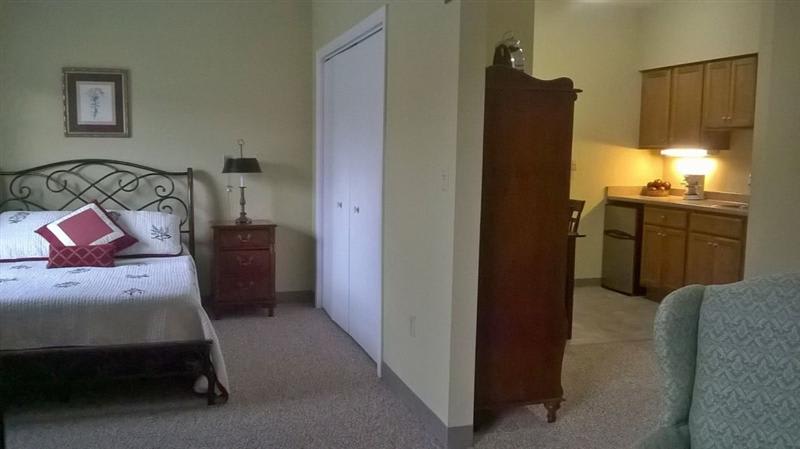 A cozy bedroom featuring a bed, wardrobe, nightstand with a lamp, and a closet.
