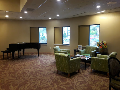 A cozy lobby featuring a piano, green chairs, and natural light from the windows.