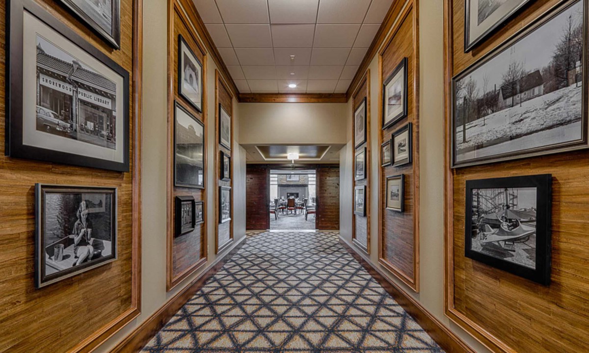 A luxurious hallway with patterned carpet and framed artwork on the walls, leading to a well-lit lounge area.