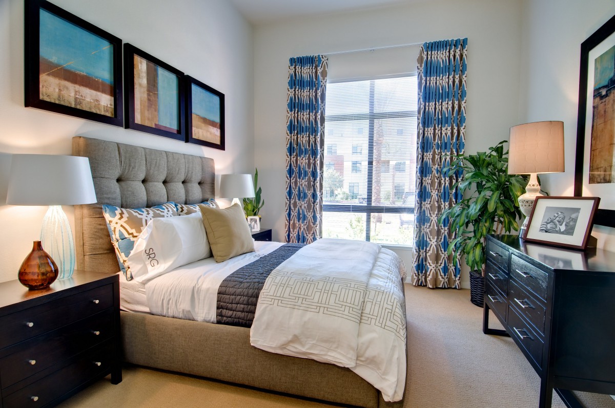 A modern bedroom with stylish decor, featuring a plush bed, vibrant curtains, and natural light streaming through a large window.