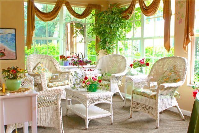 A bright and cozy sunroom featuring wicker furniture and lush indoor plants.