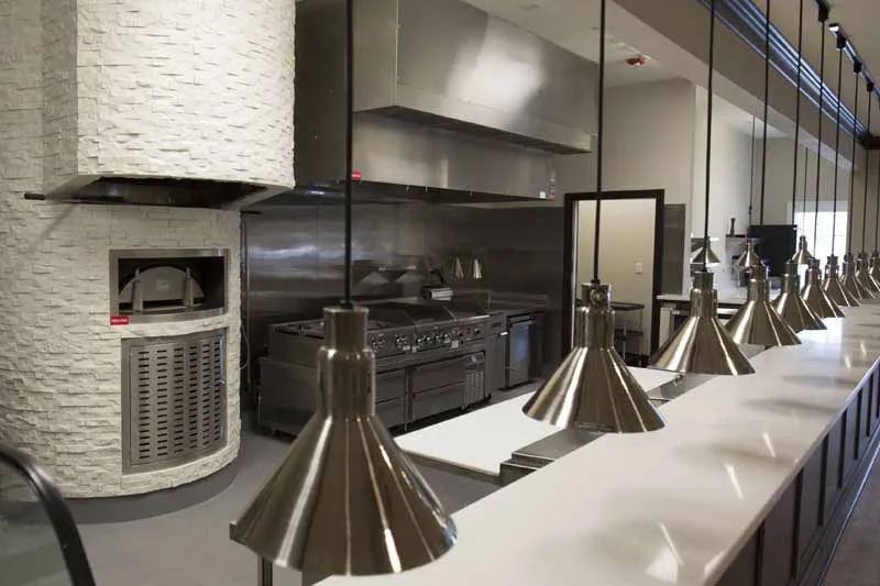 A modern restaurant kitchen with stainless steel appliances and hanging pendant lights.