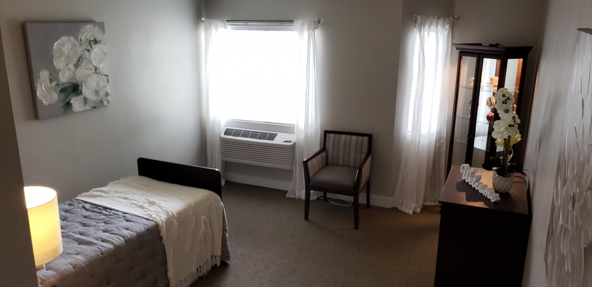 A minimalist bedroom interior with a bed, chair, and bright windows.