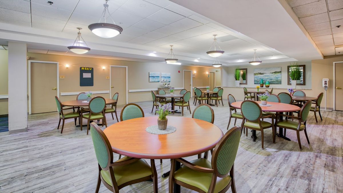 A spacious dining area featuring multiple round tables with green upholstered chairs and modern ceiling lights.