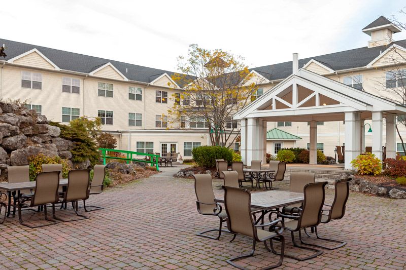 An outdoor patio area with tables and chairs, set against a multi-story building with landscaped surroundings.