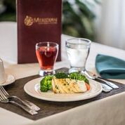 A table set with a chicken meal, accompanied by vegetables, a glass of water, and a drink at a restaurant.