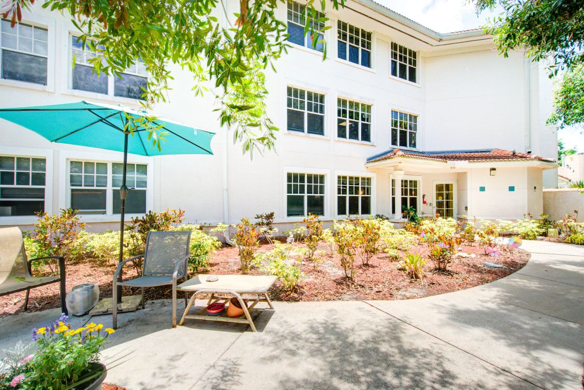 A sunny courtyard with a landscaped garden and seating area in front of a residential building.