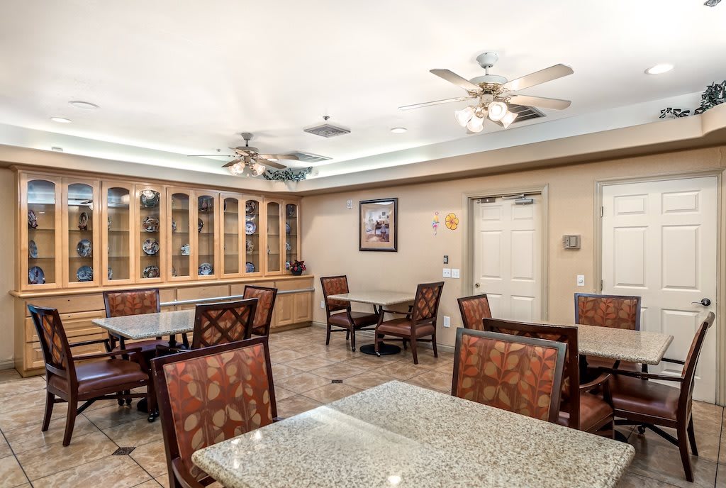A well-lit dining area with glass-top tables, cushioned chairs, and built-in cabinetry.