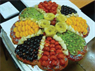 A colorful fruit tart topped with kiwi slices, blueberries, grapes, cherry tomatoes, and more.