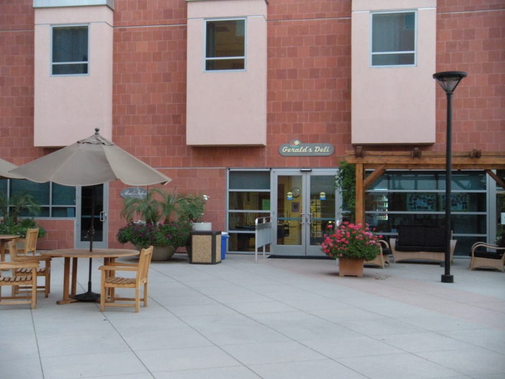 An outdoor patio area with tables, chairs, and a large umbrella in front of a building.