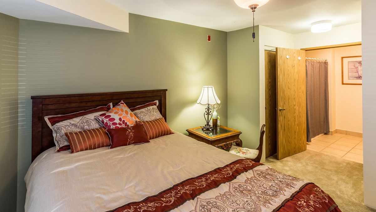 A cozy bedroom with a neatly made bed, decorative pillows, and a bedside lamp on a nightstand.