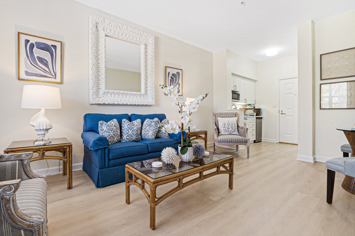 A modern living room featuring a blue sofa with decorative pillows, a stylish coffee table, and elegant decor including artwork and a large mirror.
