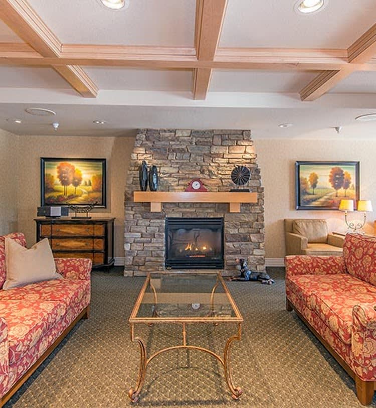 A cozy living room featuring a stone fireplace, two patterned sofas, and elegant artwork on the walls.