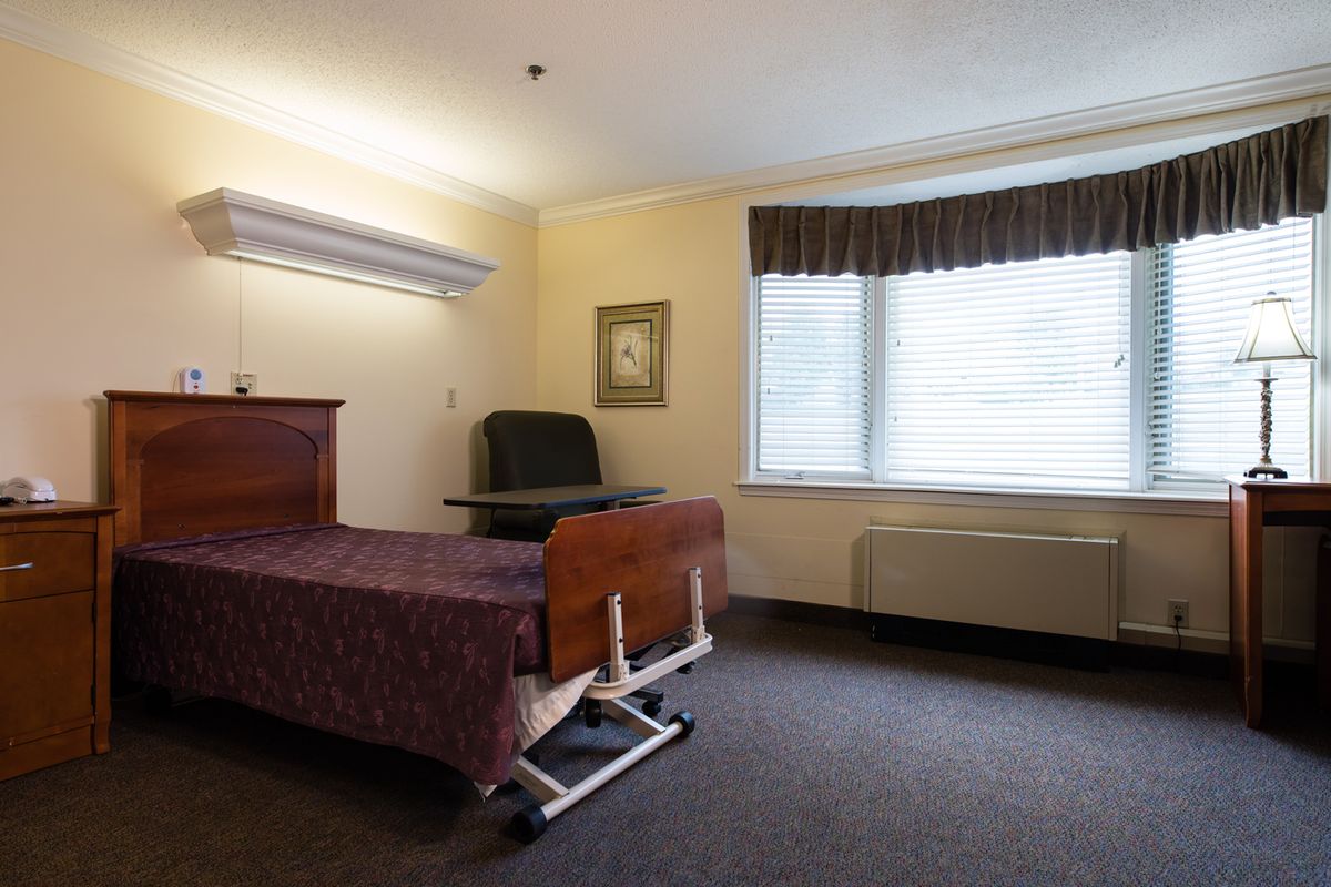 A simple, well-lit room with a hospital bed and a chair next to a window.