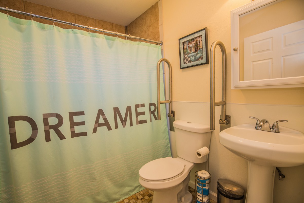 A compact bathroom featuring a toilet, sink, and a shower with a curtain displaying the word 'DREAMER'.