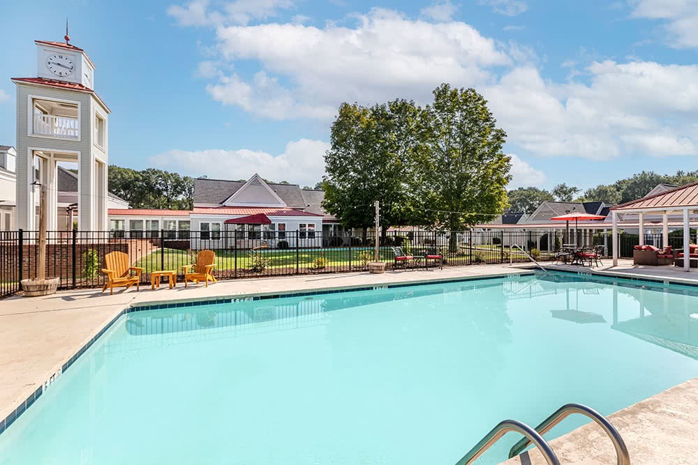 A tranquil outdoor swimming pool in a residential area, surrounded by trees and buildings under a partly cloudy sky.