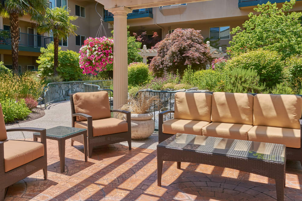 A sunny patio with comfortable seating surrounded by lush garden greenery and vibrant flowers.