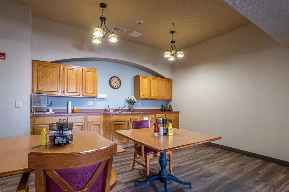 A cozy kitchen and dining area with wooden cabinets, tables, and chairs under stylish lighting fixtures.