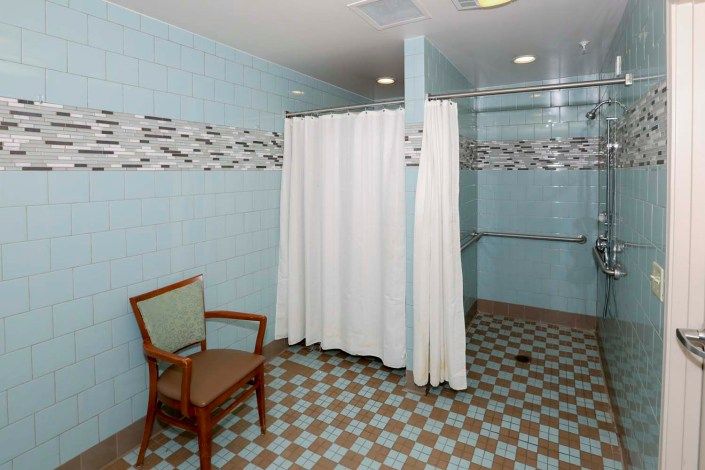 A bathroom with a shower area, featuring a curtain and a chair beside, with tiled walls.