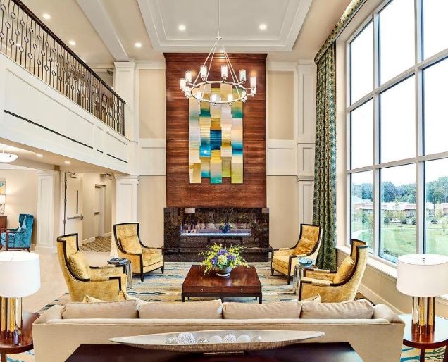 A luxurious living room featuring modern furniture, a large piece of colorful artwork, and a chandelier hanging from the high ceiling.